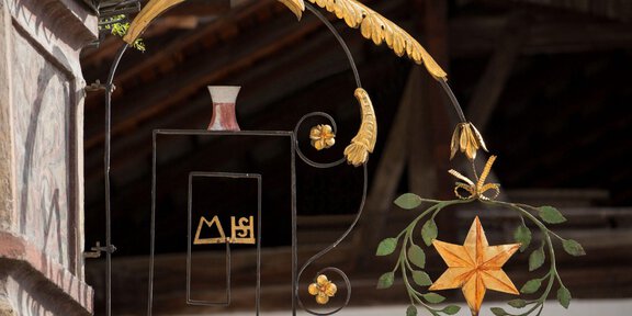 An artistically designed sign with a golden star decoration and curved embellishments. The sign hangs on a building and showcases craftsmanship. - Alter Dorfkern Oetz - Oetz