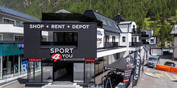 Ein modernes Sportgeschäft mit dem Namen "Sport 4 You". Es bietet Dienstleistungen wie Vermietung und Lagerung an und ist von Bergen umgeben. - Sport4You Filiale Giggijoch - Sölden