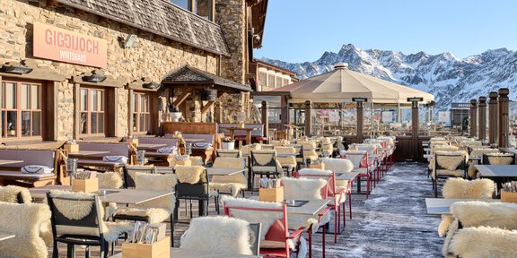 Eine gemütliche Restaurantterrasse mit Blick auf die Berge. Die Tische sind ordentlich gedeckt und mit Fellen ausgestattet. - Wirtshaus am Giggijoch - Sölden