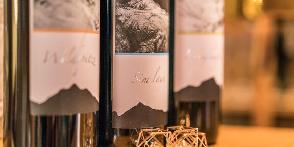 Three wine bottles with appealing labels are standing on a wooden table. Next to the bottles are elegant pieces of jewelry. - *** Appartement Pizzeria Wildspitz´ - Vent