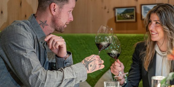 Ein Paar stößt mit Rotwein an und genießt einen gemeinsamen Moment in einem gemütlichen Restaurant. Der Tisch ist schön gedeckt, und die Atmosphäre ist freundlich und einladend. - Die Post – Wirtshaus seit 1728 - Vent