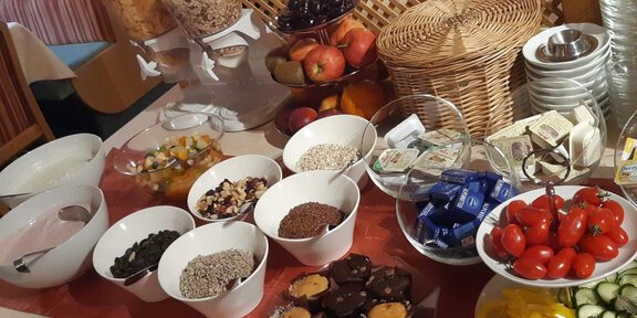 Ein reichhaltiges Frühstücksbuffet mit verschiedenen Schalen voller Obst, Joghurt, Müsli und Süßigkeiten. Dazu gibt es frische Tomaten und eine Auswahl an Zutaten. - Mein Weißkugel - Vent