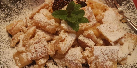 Ein Teller mit frisch zubereitetem Kaiserschmarrn, bestreut mit Puderzucker. Oben garnierte mit einem Minzblatt und einem dekorativen Schokoladenelement. - Mein Weißkugel - Vent