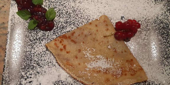 Ein leckerer Crêpe auf einem Teller, bestreut mit Puderzucker. Er ist dekoriert mit frischen Himbeeren und Minzblättern. - Mein Weißkugel - Vent