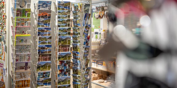 A postcard stand with many colorful postcards can be seen. In the background, a detailed shop with various souvenirs can be recognized. - Venter Kaufhäusl - Vent
