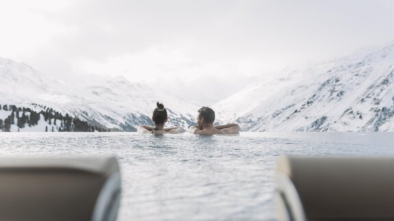 Ein Paar entspannt im Infinity-Pool mit Blick auf schneebedeckte Berge. Die ruhige Atmosphäre und die verschneite Landschaft schaffen eine entspannende Stimmung. - RIML DAS RESORT - Hochgurgl