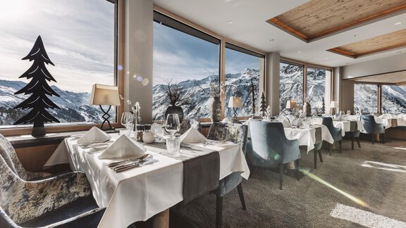 Ein elegantes Restaurant mit großen Fenstern und Blick auf die schneebedeckten Berge. Die Tische sind stilvoll gedeckt und die Umgebung ist gemütlich. - SKI | GOLF | WELLNESS Hotel Riml - Hochgurgl