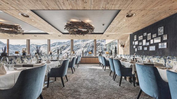 Ein elegantes Restaurant mit blauen Stühlen und großen Fenstern, die einen Blick auf die Berge bieten. Der Innenraum ist modern und gemütlich eingerichtet. - SKI | GOLF | WELLNESS Hotel Riml - Hochgurgl