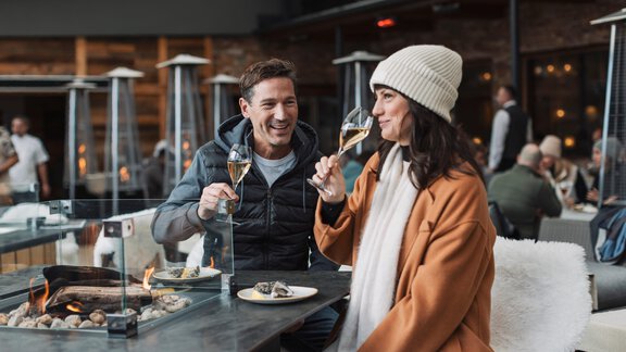 Ein Paar genießt Sekt und kleine Speisen an einem modernen Tisch. Die Umgebung wirkt gemütlich und einladend mit einer feierlichen Atmosphäre. - SKI | GOLF | WELLNESS Hotel Riml - Hochgurgl