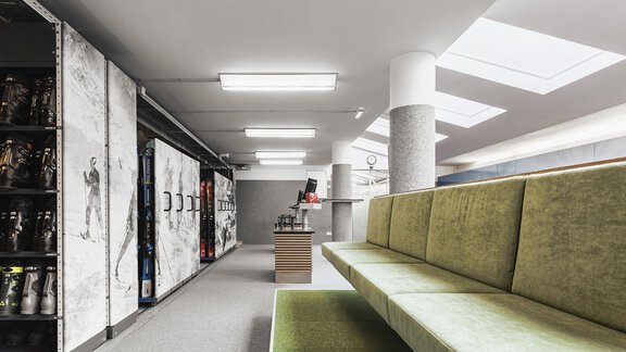 Ein moderner Raum mit grünem Sitzbereich und großen Fenstern. Im Hintergrund sind Schließfächer und eine Empfangstheke sichtbar. - SKI | GOLF | WELLNESS Hotel Riml - Hochgurgl