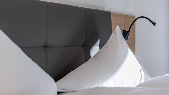 Ein modernes Kopfteil mit einer gemütlichen Lichtquelle. Auf dem Bett liegen zwei große Kissen. - Alpenappartement Central Valley Penthouse - Längenfeld