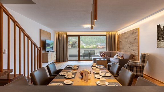 Ein modernes Wohnzimmer mit einem großen Esstisch und elegantem Mobiliar. Fenster ermöglichen einen Blick nach draußen auf eine Terrasse. - Alpenappartement Central Valley Penthouse - Längenfeld