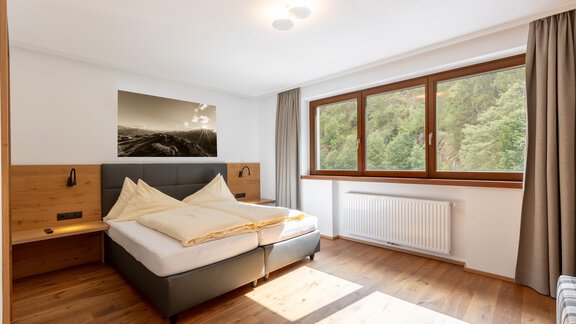 Ein modernes Schlafzimmer mit einem großen Fenster und Blick auf die Natur. Es gibt ein Doppelbett mit gemütlichen Kissen und Holzdetails. - Alpenappartement Central Valley Penthouse - Längenfeld