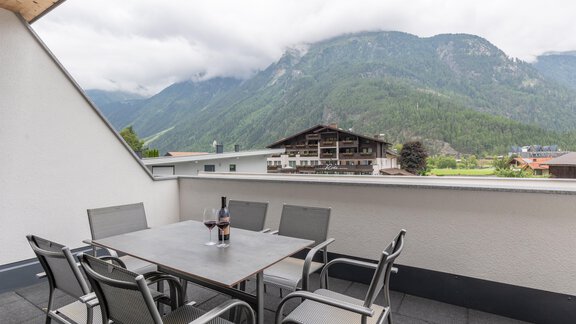 Eine gemütliche Terrasse mit einem Tisch und Stühlen, ideal zum Entspannen. Im Hintergrund sind beeindruckende Berge und ein bewölkter Himmel zu sehen. - Alpenappartement Central Valley Penthouse - Längenfeld