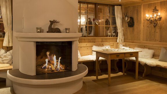 A cozy room with a fireplace and wooden paneling. A table is festively set and there are comfortable seating options. - Art & Relax Hotel Bergwelt - Obergurgl 