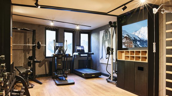 A modern home gym with various training equipment. Large windows offer a view of the mountains. - Art & Relax Hotel Bergwelt - Obergurgl 