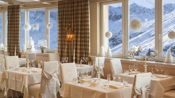 An elegant restaurant with festive table decorations and a view of snowy mountains. Large windows allow plenty of daylight in, creating a cozy atmosphere. - Art & Relax Hotel Bergwelt - Obergurgl 