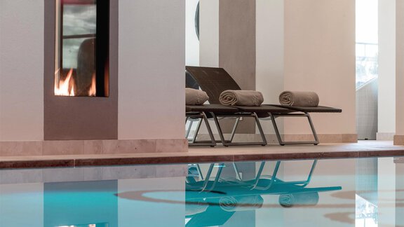 An elegant spa area with a modern swimming pool. In the background, there are loungers and a fireplace. - Art & Relax Hotel Bergwelt - Obergurgl 