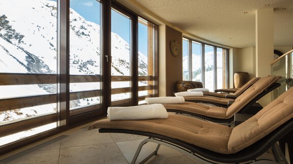 A relaxing wellness area with comfortable loungers and large windows. Visible outside are snow-covered mountains under a clear blue sky. - Art & Relax Hotel Bergwelt - Obergurgl 