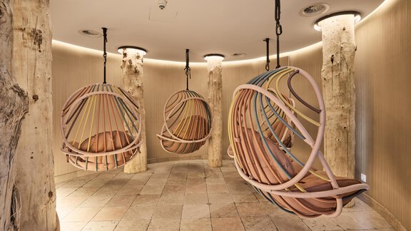 A cozy room with hanging wooden swings and colorful accents. The walls are in warm tones, while natural wooden elements are present in the room. - Art & Relax Hotel Bergwelt - Obergurgl 
