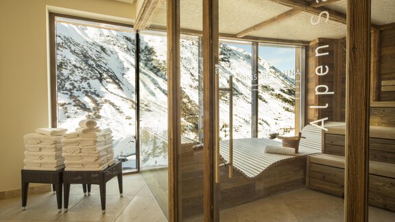 A modern wellness area with large windows overlooking snow-capped mountains. White towels are neatly stacked and there are comfortable loungers for relaxation. - Art & Relax Hotel Bergwelt - Obergurgl 