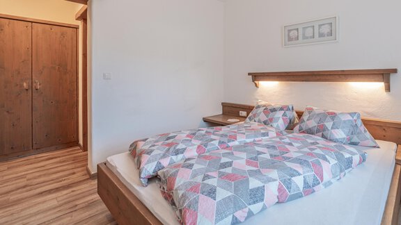 Ein gemütliches Schlafzimmer mit einem großen Bett und bunten Decken. Es gibt einen Holzschrank und eine ruhige, helle Atmosphäre. - Ferienwohnung Alt Poschach - Obergurgl 