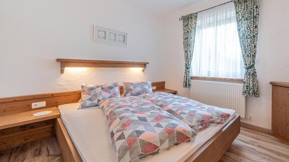 Ein gemütliches Schlafzimmer mit einem großen Doppelbett und Holzdetails. Die Fenster sind mit Vorhängen geschmückt und der Raum wirkt hell und einladend. - Ferienwohnung Alt Poschach - Obergurgl 