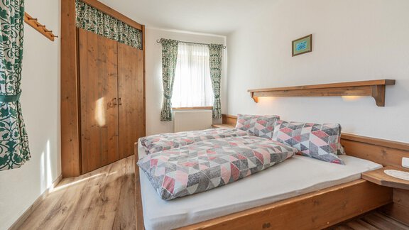 Ein gemütliches Schlafzimmer mit einem Doppelbett und bunten Bettdecken. Der Raum hat Holzfußboden und große Fenster mit Vorhängen. - Ferienwohnung Alt Poschach - Obergurgl 
