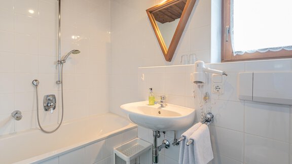 Ein modernes Badezimmer mit einer Badewanne und einer Dusche. Die Wände sind hell gefliest, und es gibt ein Waschbecken mit einem großen Spiegel. - Ferienwohnung Alt Poschach - Obergurgl 