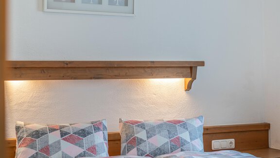 Ein gemütliches Schlafzimmer mit einem Doppelbett und bunten Kissen. An der Wand hängt ein gerahmtes Bild, und die Beleuchtung sorgt für eine warme Atmosphäre. - Ferienwohnung Alt Poschach - Obergurgl 