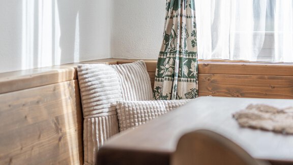 Ein gemütlicher Raum mit einer Holzbank und einem Tisch. Helle Vorhänge lassen viel Licht herein und schaffen eine einladende Atmosphäre. - Ferienwohnung Alt Poschach - Obergurgl 