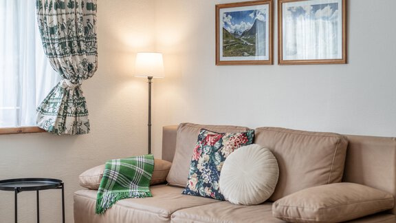 Ein gemütliches Wohnzimmer mit einem beigen Sofa und bunten Kissen. An der Wand hängen Bilder und es gibt eine Stehlampe neben dem Sofa. - Ferienwohnung Alt Poschach - Obergurgl 