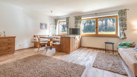 Ein helles Wohnzimmer mit einem großen Teppich, bequemen Möbeln und Fenstern, die auf die Natur blicken. Die Einrichtung ist gemütlich und einladend. - Ferienwohnung Alt Poschach - Obergurgl 