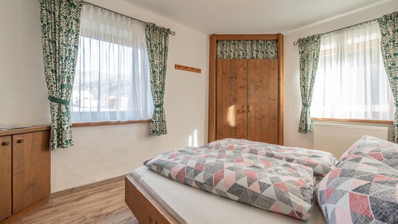 Ein gemütliches Schlafzimmer mit zwei Betten und bunten Kissen. Die Fenster sind mit hellen Vorhängen dekoriert und der Raum hat Holzmöbel. - Ferienwohnung Alt Poschach - Obergurgl 