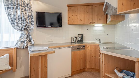 Eine moderne Küchenzeile aus Holz mit einem kleinen Essbereich. Die Wände sind hell, und es gibt eine Fensterbank mit Vorhängen. - Ferienwohnung Alt Poschach - Obergurgl 