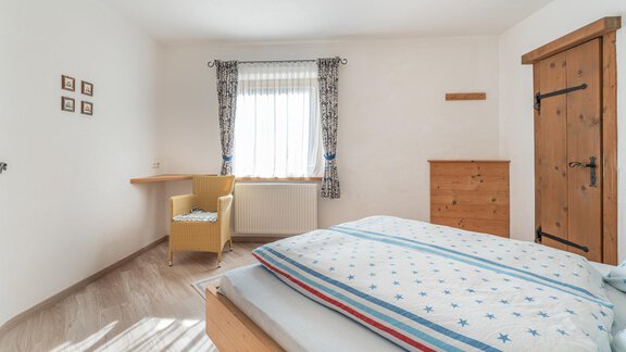 Ein gemütliches Schlafzimmer mit einem großen Bett und blauen Bettwäsche. Es gibt einen Schreibtisch, einen Stuhl und ein Holzschrank, alles in schlichtem Design. - Ferienwohnung Alt Poschach - Obergurgl 