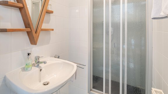 Ein modernes Badezimmer mit einem Waschbecken und einer Duschkabine. Die Wände sind hell gefliest und es gibt Holzregale für Toilettenartikel. - Ferienwohnung Alt Poschach - Obergurgl 