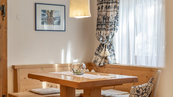 Ein gemütlicher Essbereich mit einem Holztisch und Bänken. Die Fenster sind mit Vorhängen geschmückt, und eine Lampe sorgt für warmes Licht. - Ferienwohnung Alt Poschach - Obergurgl 