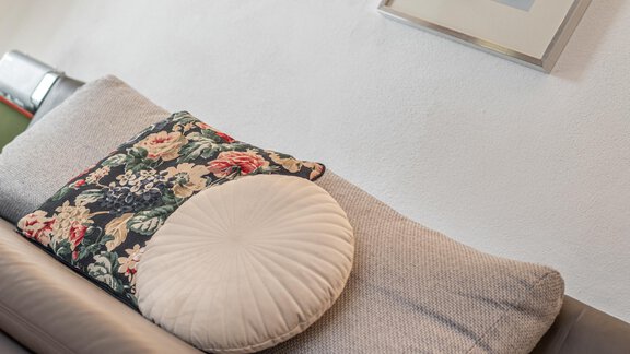 Ein modernes Sofa mit einem runden Kissen und einem dekorativen, blumenmuster Kissen. An der Wand hängt ein gerahmtes Bild. - Ferienwohnung Alt Poschach - Obergurgl 