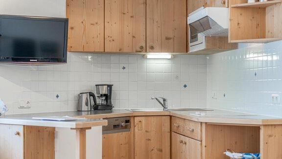 Eine moderne Küche mit Holzschränken und einem Fernseher an der Wand. Die Ausstattung umfasst eine Kaffeemaschine und eine Spüle. - Ferienwohnung Alt Poschach - Obergurgl 