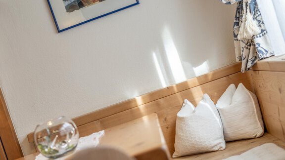 Ein gemütlicher Wohnbereich mit Holzdetails. An der Wand hängt ein Bild, und auf der Bank liegen komfortable Kissen. - Ferienwohnung Alt Poschach - Obergurgl 