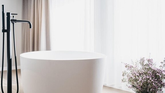 A modern bathroom with an elegant, freestanding bathtub and a black faucet. Next to the bathtub stands an elegant flower vase with fresh flowers. - The Crystal VAYA Unique - Obergurgl 