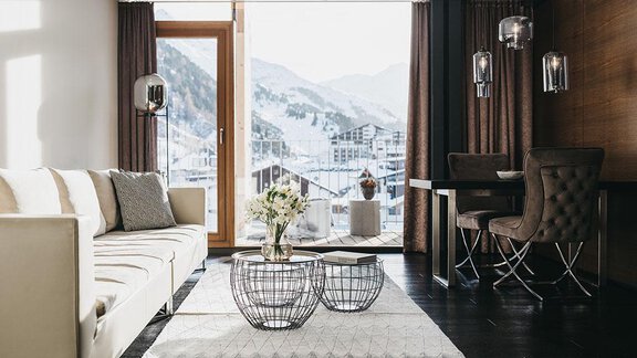 A modern living room with a white sofa and elegant furniture. The large windows offer a view of a snowy mountain landscape. - The Crystal VAYA Unique - Obergurgl 