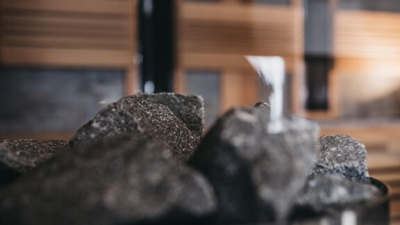 A close-up of dark stones on a sauna stove. Wooden-paneled walls can be seen in the background. - The Crystal VAYA Unique - Obergurgl 