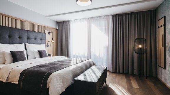 A modern bedroom with a large bed and soft pillows. Bright curtains and wooden flooring create a cozy atmosphere. - The Crystal VAYA Unique - Obergurgl 