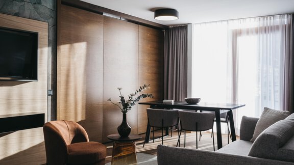 A modern living room with a cozy sofa, a table, and chairs. Large windows let in plenty of light and create an inviting atmosphere. - The Crystal VAYA Unique - Obergurgl 