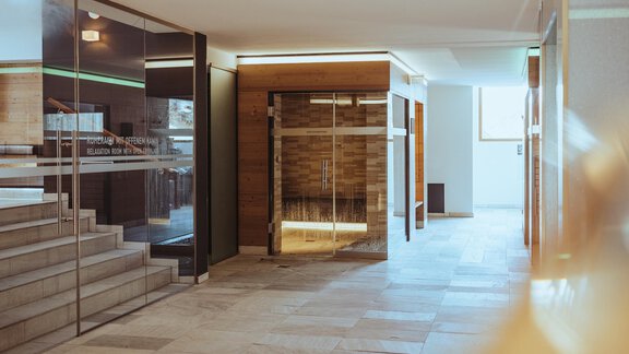 A modern interior with a bright, open area. On the left side, there are glass walls and a staircase, while on the right side, a sauna is visible. - The Crystal VAYA Unique - Obergurgl 