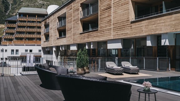 A modern hotel with a wooden façade and cozy terrace furniture. The pool area is inviting and offers a beautiful view of the surrounding mountains. - The Crystal VAYA Unique - Obergurgl 