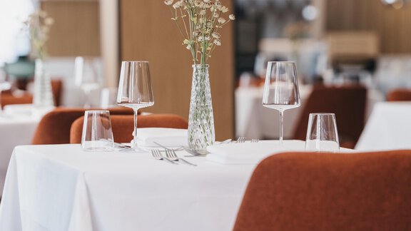 An elegant restaurant with beautifully set tables. The tables are set in white and decorated with vase flowers. - The Crystal VAYA Unique - Obergurgl 
