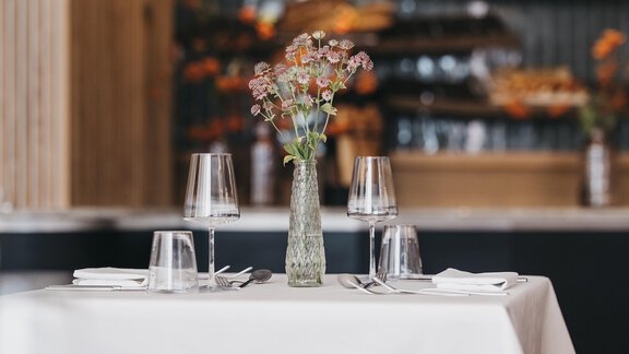 An elegant table in a restaurant, decorated with a vase full of flowers. Glassware is placed on the table, and the atmosphere is cozy. - The Crystal VAYA Unique - Obergurgl 